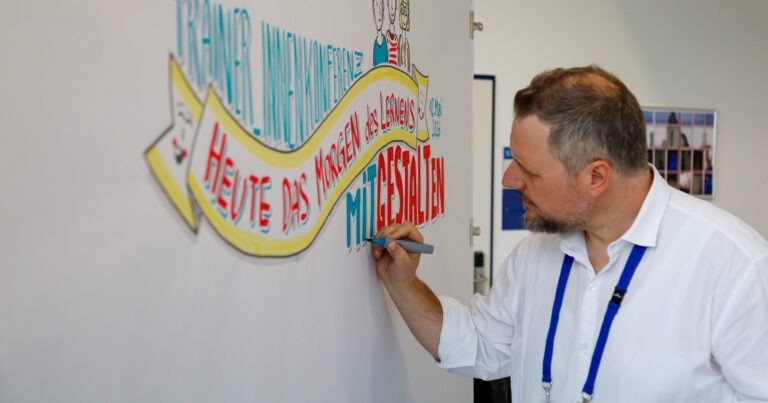 Graphic Recording: Harald Karrer zeichnet live das Motto der Trainer:innenkonferenz an die Wand
